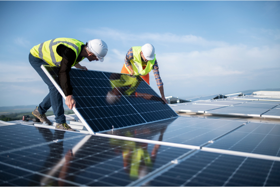 Two worker with hardhats holding solar panel on a rooftop